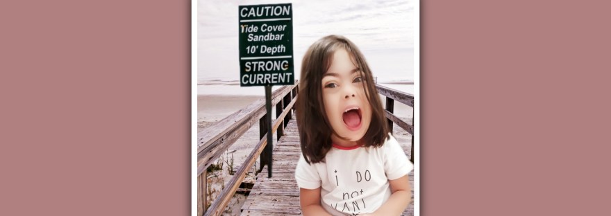 imagen niña sindrome de down en playa con cartel de precaucion