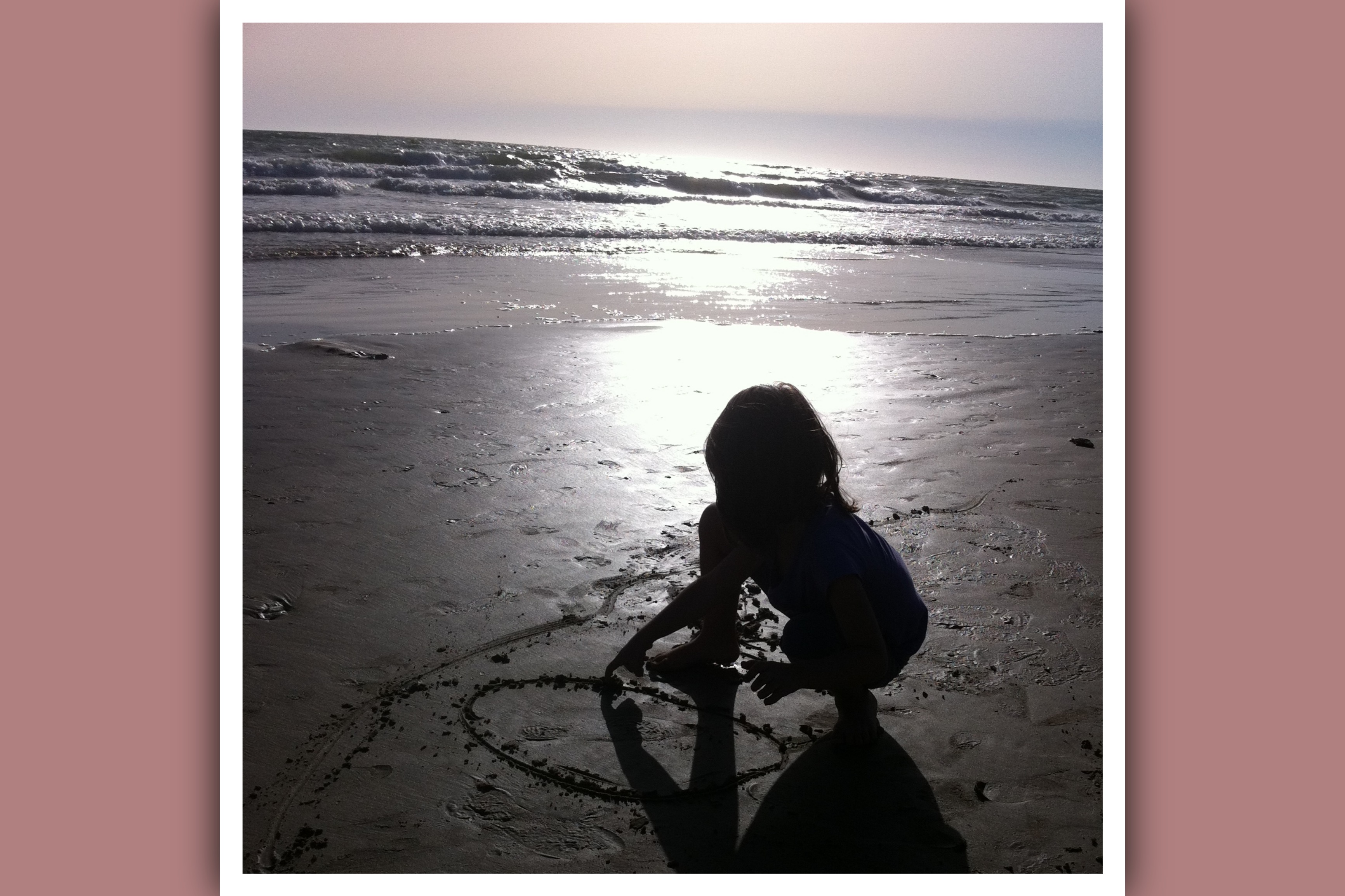 niña en la playa al atardecer dibujando un circulo en la arena